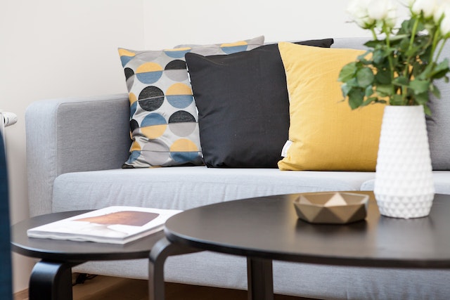 close up of a grey couch with yellow and blue throw pillows and dark wood coffee table
